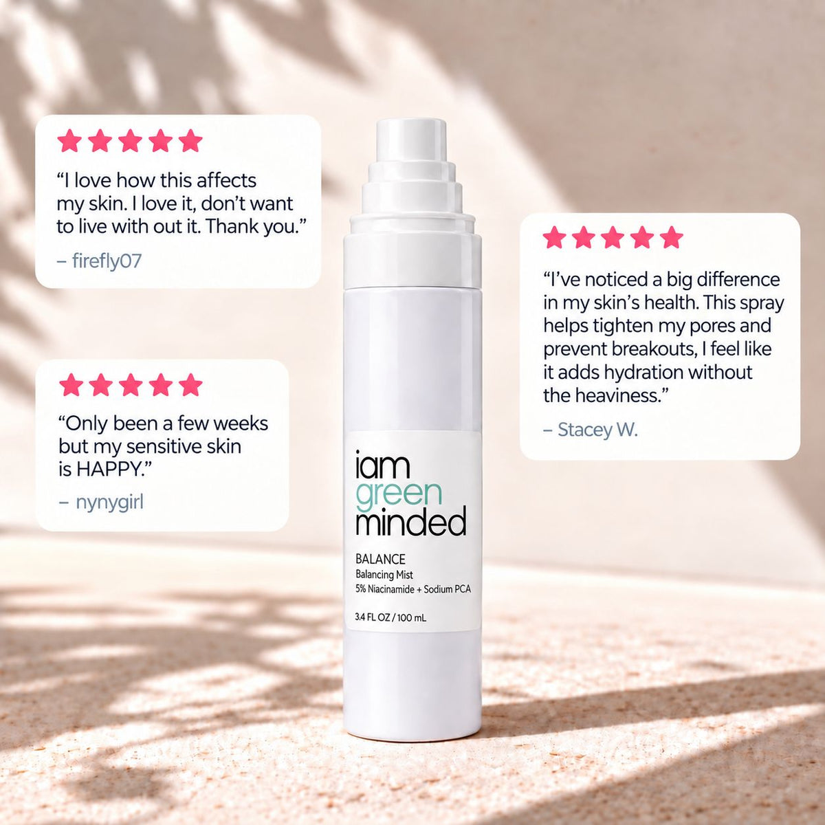 A white spray bottle labeled 'iam green minded' stands centered on a sandy surface with two white review cards and star ratings beside it. The scene is softly lit with warm sunlight and shadows.