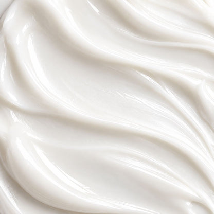 A close-up texture shot of a thick, creamy white cosmetic cream with smooth, flowing swirls and soft highlights.