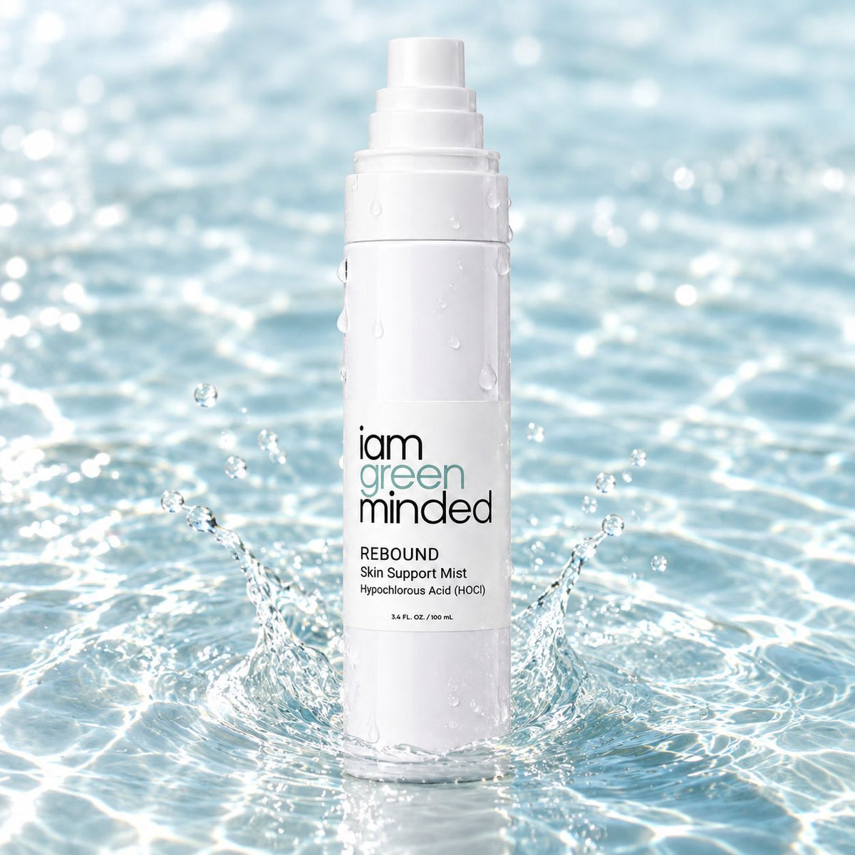 A white bottle of iam green minded REBOUND Skin Support Mist stands in splashing water, with droplets on the bottle and a bright blue water background.