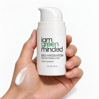 Hand holding iamgreenminded BIO-HYDRATION Barrier Moisturizer with a white cream swatch on the skin against a white studio background.